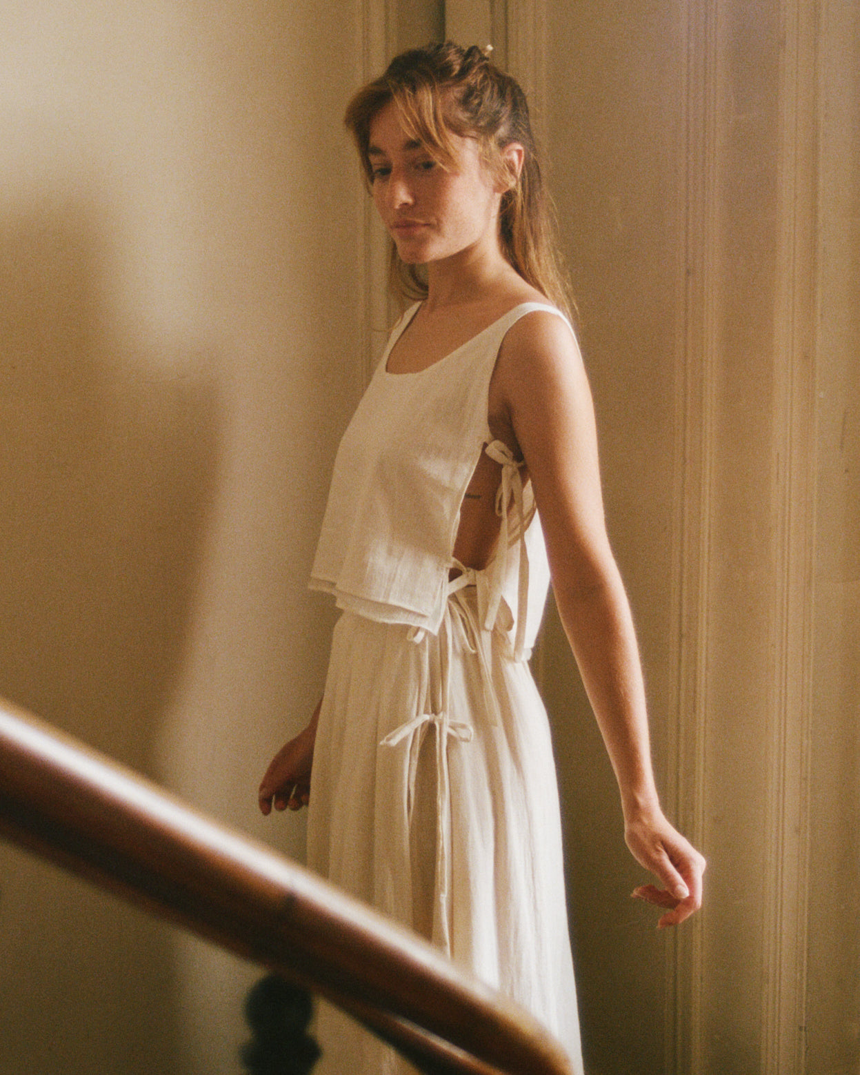 Model wearing white Lacets Top showing the adjustable side ties. Styled with The Pleated Skirt, perfect for Summer.