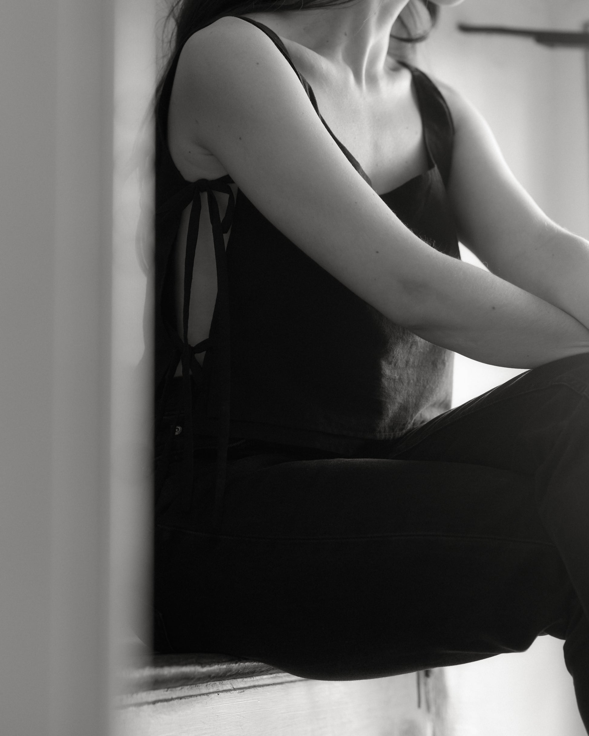 Model sitting on stairs wearing black Lacets Top ,showing the adjustable side ties. 